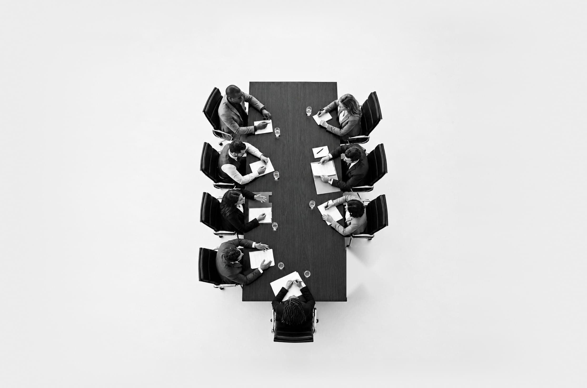 Top-down view of a boardroom table with executives seated around it and two empty chairs